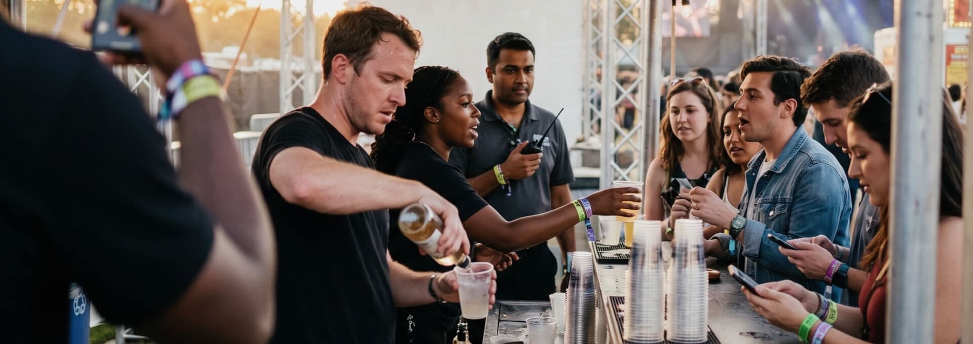 Bartender smiling while pouring and serving beverages to attendees at a crowded festival bar